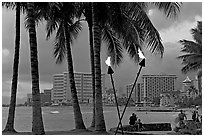 Waterfront at dusk with bare flame lamps. Waikiki, Honolulu, Oahu island, Hawaii, USA (black and white)