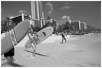 Women carrying surfboards into the water, Waikiki Beach. Waikiki, Honolulu, Oahu island, Hawaii, USA (black and white)