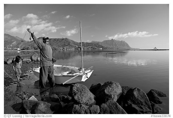 Fisherman pulling out fish out a net, with girl looking, Kaneohe Bay, morning. Oahu island, Hawaii, USA (black and white)