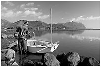 Fisherman pulling out fish out a net, with girl looking, Kaneohe Bay, morning. Oahu island, Hawaii, USA (black and white)