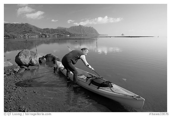 Man loading sea kayak for a fishing trip, Kaneohe Bay, morning. Oahu island, Hawaii, USA (black and white)