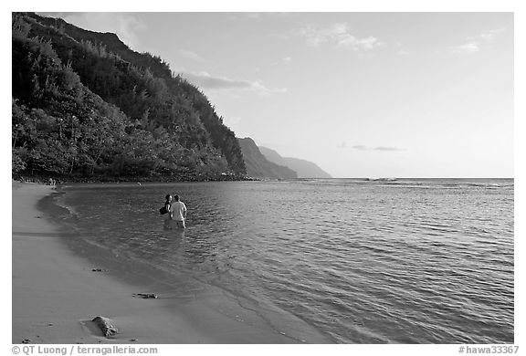 Couple standing in water looking at the Na Pali Coast, Kee Beach, late afternoon. Kauai island, Hawaii, USA