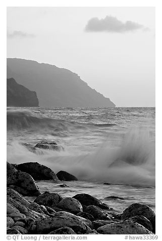 Boulders, waves, and Na Pali cliffs, sunset. Kauai island, Hawaii, USA