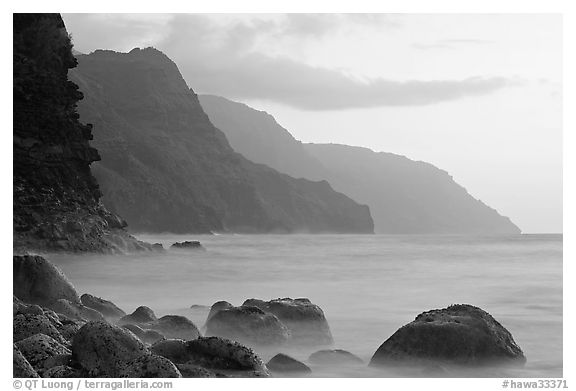 Boulders, surf, and Na Pali cliffs, sunset. Kauai island, Hawaii, USA