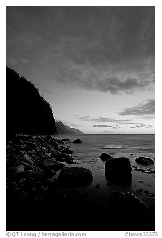 Boulders, surf, and Na Pali cliffs, dusk. North shore, Kauai island, Hawaii, USA (black and white)