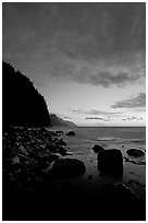 Boulders, surf, and Na Pali cliffs, dusk. North shore, Kauai island, Hawaii, USA (black and white)