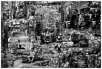 Boy sits next to large stone smiling faces, the Bayon. Angkor, Cambodia ( black and white)