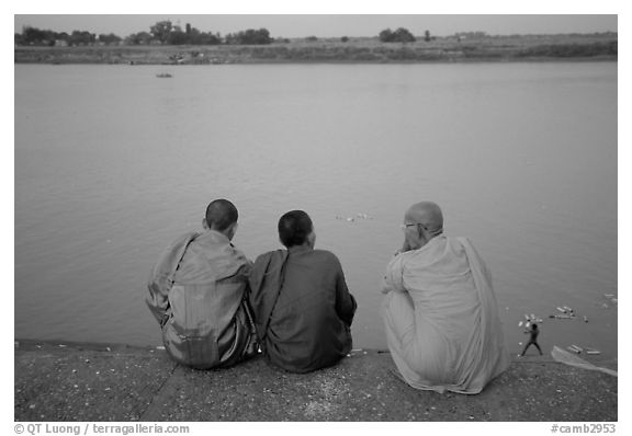 Buddhist monks sit on  banks of Tongle Sap river at dusk,  Phnom Phen. Cambodia (black and white)