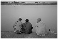 Buddhist monks sit on  banks of Tongle Sap river at dusk,  Phnom Phen. Cambodia (black and white)