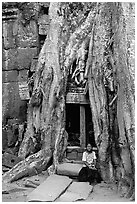 Girl sits at the base of huge bayan tree encroaching on ruins in Ta Prom. Angkor, Cambodia (black and white)