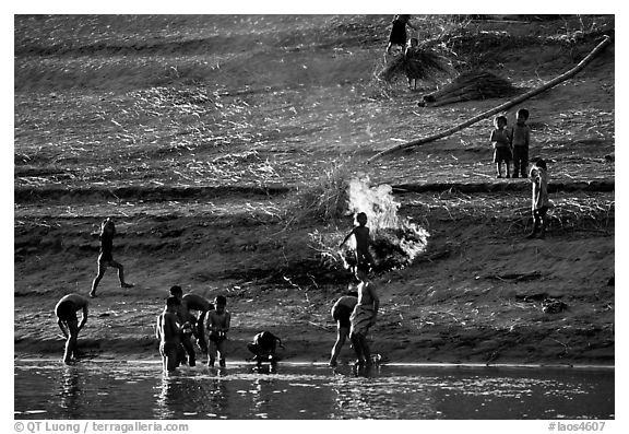 Children bathe in the river and dry out near a fire in a small hamlet. Mekong river, Laos (black and white)