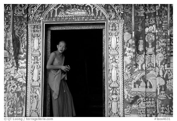 Buddhist novice monk stands at door of shrine, Wat Xieng Thong. Luang Prabang, Laos