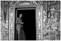 Buddhist novice monk stands at door of shrine, Wat Xieng Thong. Luang Prabang, Laos (black and white)