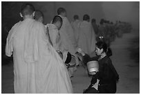 Woman gives alm during morning procession of buddhist monks. Luang Prabang, Laos (black and white)