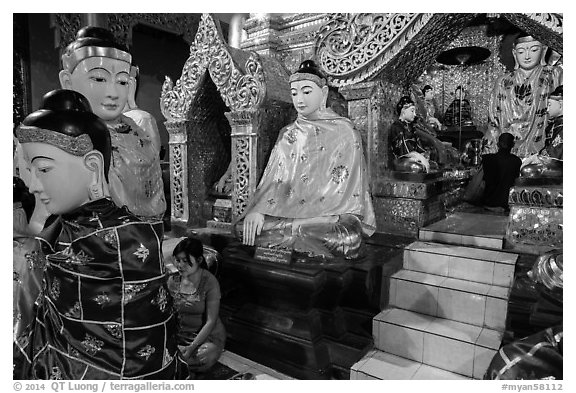 Woman and monk in pavillion surrounded by Buddha statues. Yangon, Myanmar (black and white)