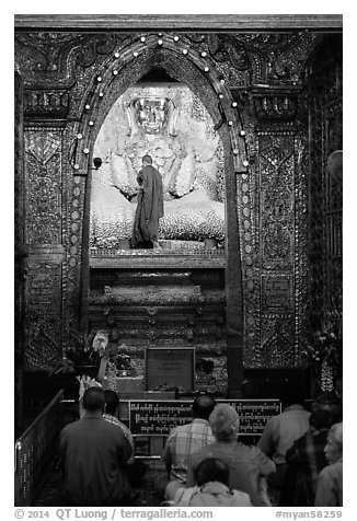 Monk applying gold leaf to Buddha statue in Mahamuni Pagoda. Mandalay, Myanmar (black and white)