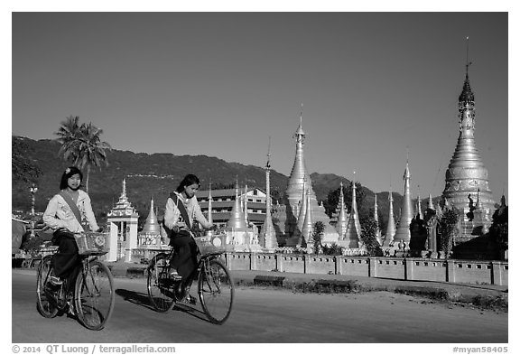 Schoolgirls riding bicycles past golden stupas. Pindaya, Myanmar (black and white)