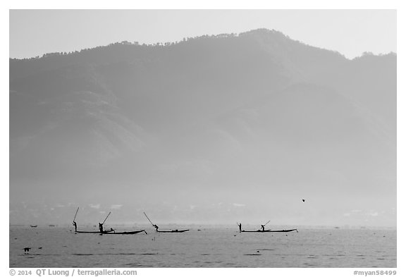 Intha fishermen in the distance using spears to stir fish, below tall hills. Inle Lake, Myanmar (black and white)