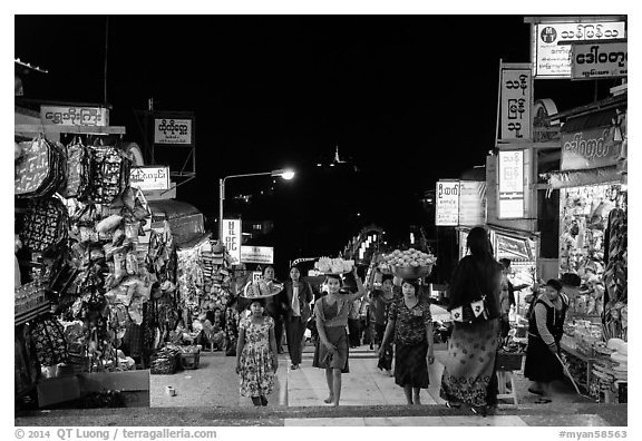 Girls carry offering material up the stairs of Potemkin village at night. Kyaiktiyo, Myanmar (black and white)