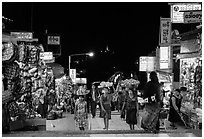 Girls carry offering material up the stairs of Potemkin village at night. Kyaiktiyo, Myanmar ( black and white)