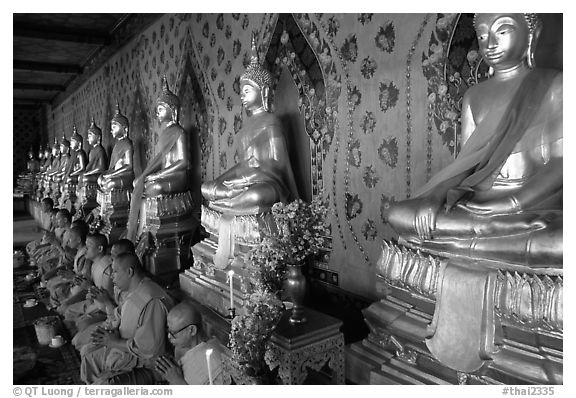 Monks sitting below row of buddha images, Wat Arun. Bangkok, Thailand (black and white)