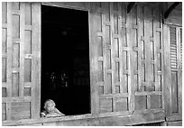 Woman looks out of teak house window. Damonoen Saduak, Thailand (black and white)