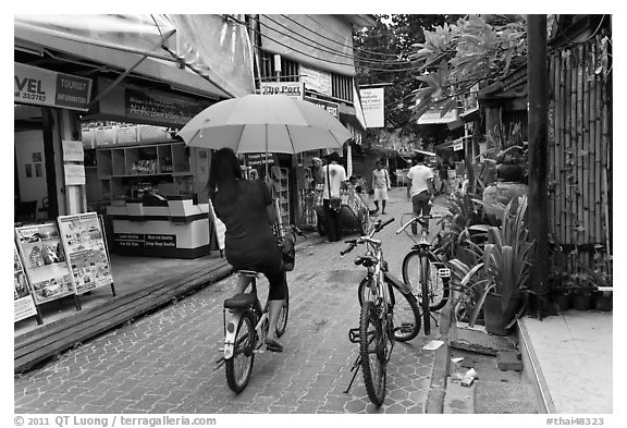 Woman riding bicycle with unbrella, Tonsai village, Ko Phi-Phi Don. Krabi Province, Thailand (black and white)