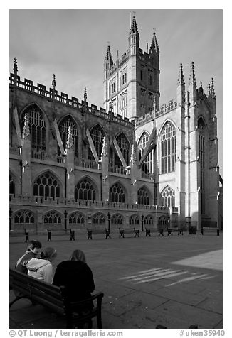 Young people sitting on a bench in a square below Bath Abbey. Bath, Somerset, England, United Kingdom (black and white)