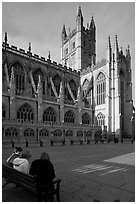 Young people sitting on a bench in a square below Bath Abbey. Bath, Somerset, England, United Kingdom (black and white)