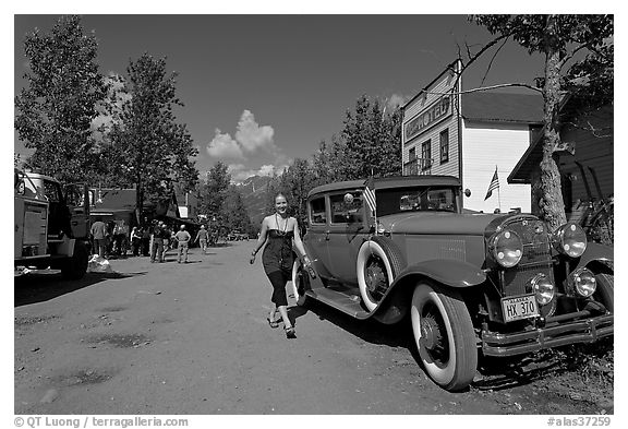 Woman walking next to red classic car. McCarthy, Alaska, USA (black and white)