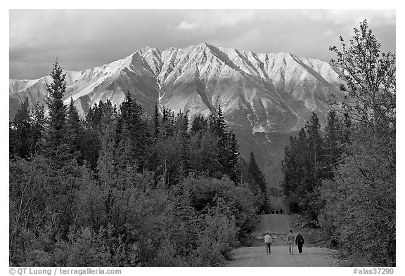 People walking on unpaved road, with last light on mountains. McCarthy, Alaska, USA (black and white)