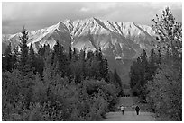 People walking on unpaved road, with last light on mountains. McCarthy, Alaska, USA ( black and white)