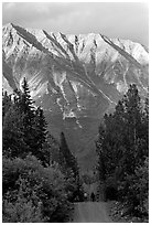 People strolling on unpaved path, with sunset light on mountains. McCarthy, Alaska, USA (black and white)