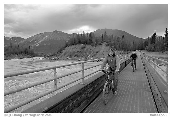 Mountain bikers crossing Kennicott River Footbridge at sunset. McCarthy, Alaska, USA (black and white)