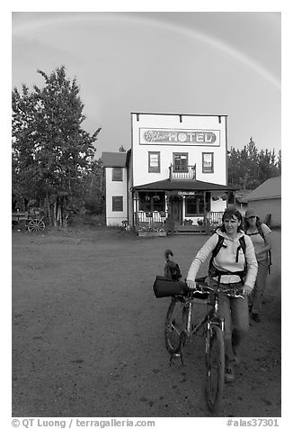 Women with bikes, hotel, and rainbow. McCarthy, Alaska, USA (black and white)