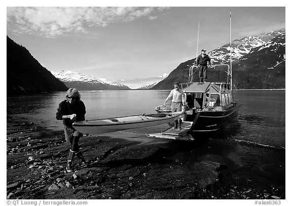 Man and woman carry kayak out of small boat at Black Sand Beach. Prince William Sound, Alaska, USA (black and white)