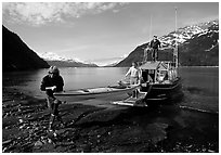 Man and woman carry kayak out of small boat at Black Sand Beach. Prince William Sound, Alaska, USA (black and white)