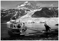 Man and woman  unload  kayak from the water taxi boat at Black Sand Beach. Prince William Sound, Alaska, USA ( black and white)