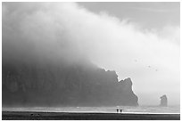 Two people strolling on the beach at the base of Morro Rock. Morro Bay, USA (black and white)