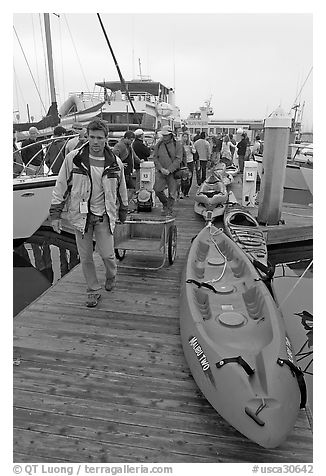 Sea kayaks and passengers awaiting loading on tour boat. California, USA (black and white)