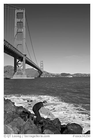 Surfer scrambling on rocks below the Golden Gate Bridge. San Francisco, California, USA (black and white)