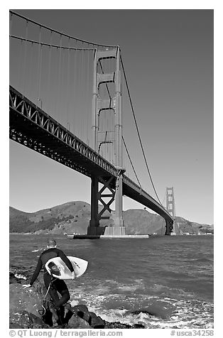 Surfer stepping on rocks and Golden Gate Bridge. San Francisco, California, USA