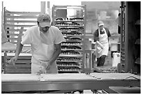 Baker hand-coating lofs of bread. San Francisco, California, USA (black and white)