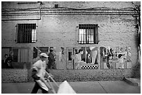 Man pushing a cart in front of mural paintings, Ross Alley, Chinatown. San Francisco, California, USA ( black and white)