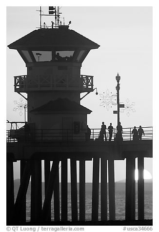 People and pier silhouetted by the setting sun. Huntington Beach, Orange County, California, USA