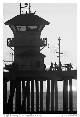 People and pier silhouetted by the setting sun. Huntington Beach, Orange County, California, USA (black and white)