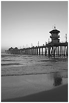 Huntington Pier and reflections in wet sand at sunset. Huntington Beach, Orange County, California, USA (black and white)