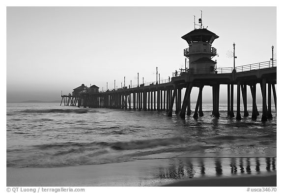 The 1853 ft Huntington Pier reflected in wet sand at sunset. Huntington Beach, Orange County, California, USA (black and white)