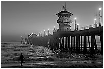 Surfer and Huntington Pier lights at twilight. Huntington Beach, Orange County, California, USA ( black and white)