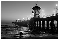 Surfer entering water next to the Huntington Pier, sunset. Huntington Beach, Orange County, California, USA ( black and white)
